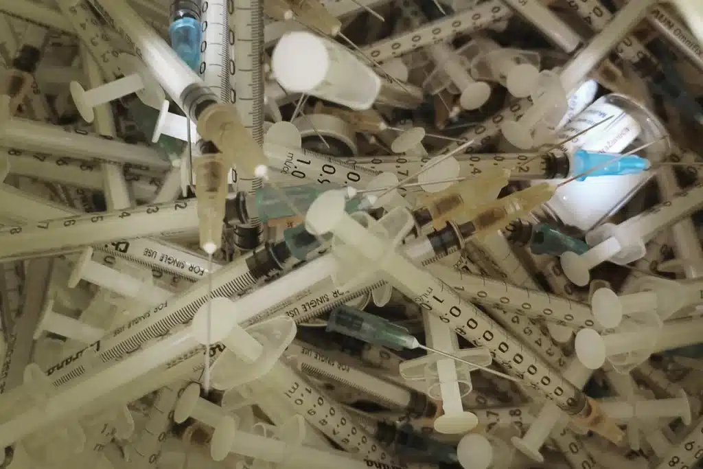 A large pile of used, discarded syringes, needles, and vials (sharps waste)
