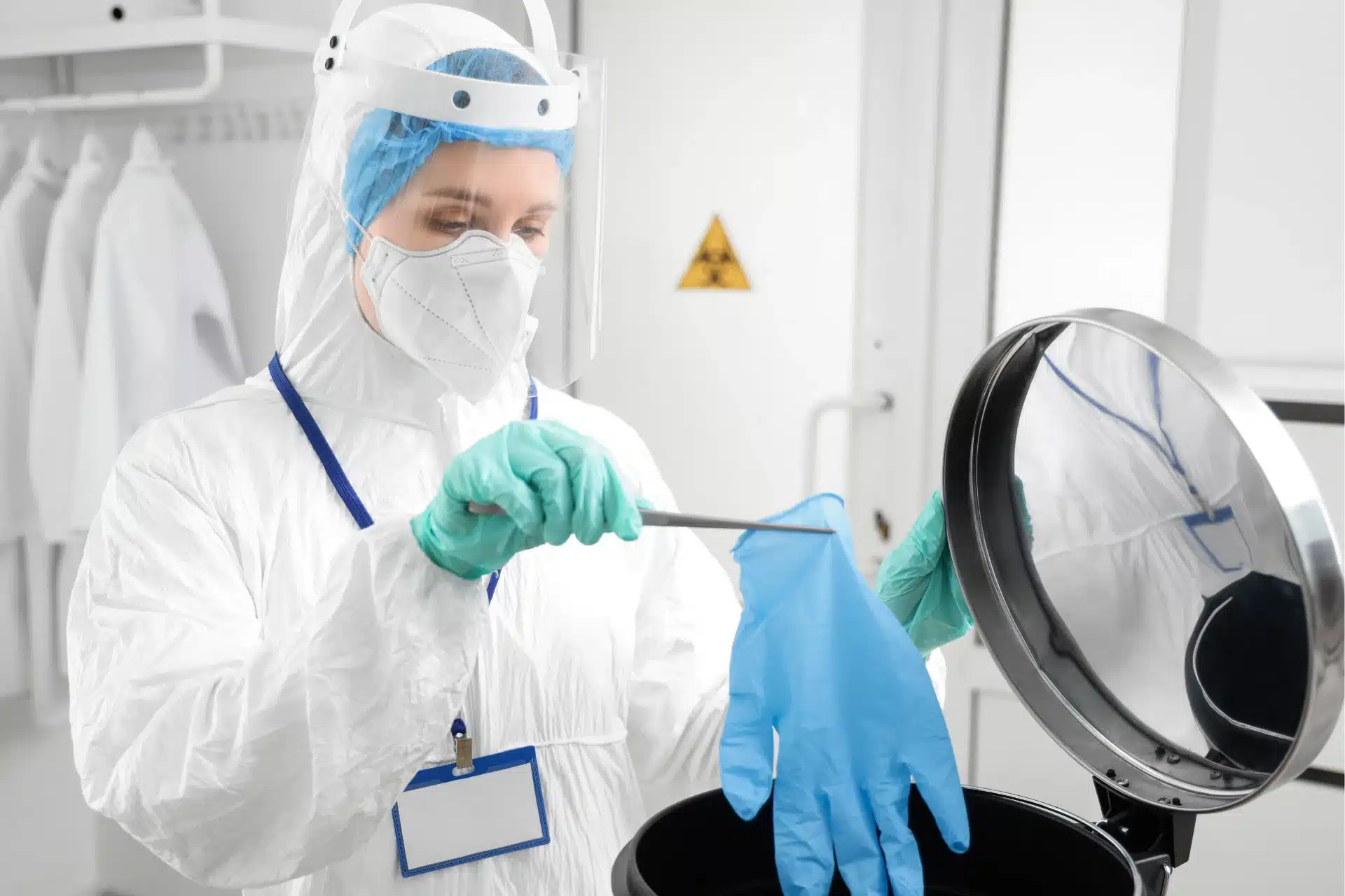 Medical worker in protective uniform throwing used gloves into waste container in a clinic 