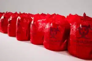 A row of red biohazard waste bags lined up side by side, each marked with a biohazard symbol and “Biohazard Infectious Waste” text