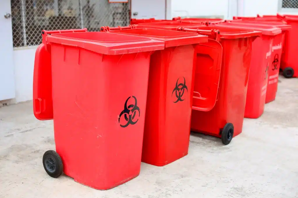 Row of large red wheeled waste bins marked with biohazard symbols lined up outside a building