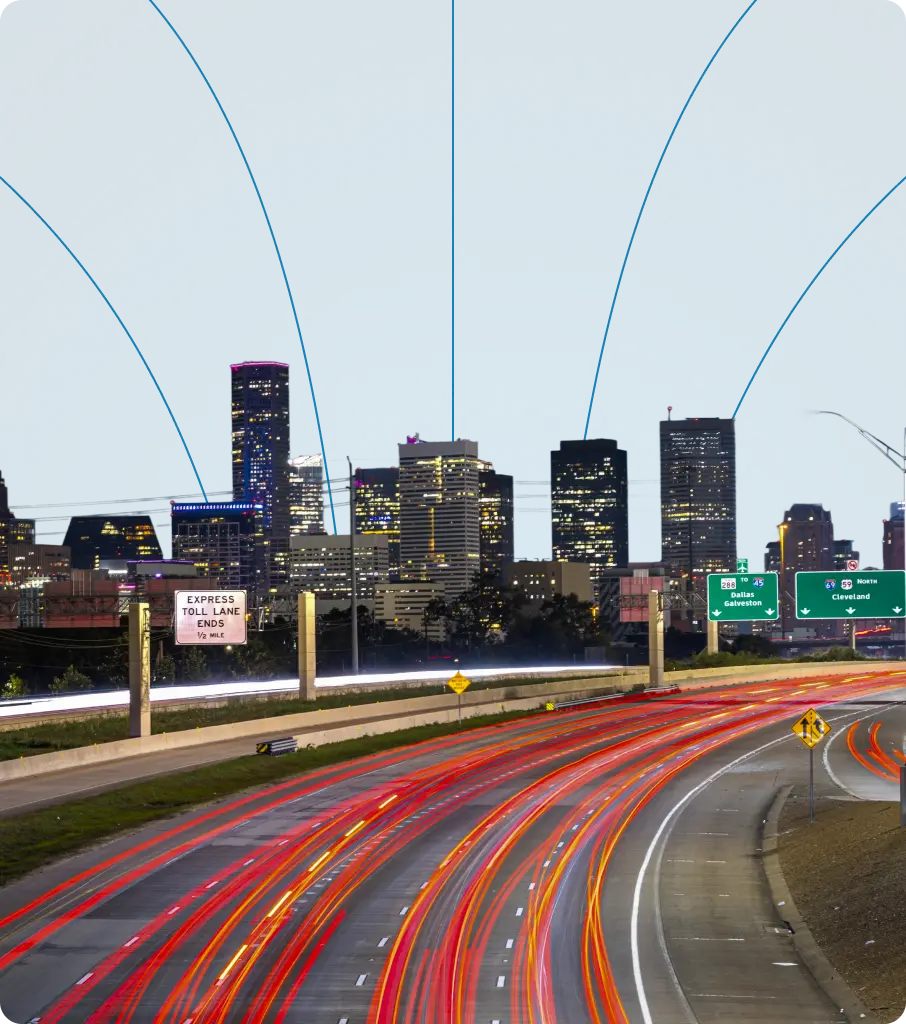 Houston downtown skyline at dusk from highway with light trails, showing illuminated office buildings and roadway signage