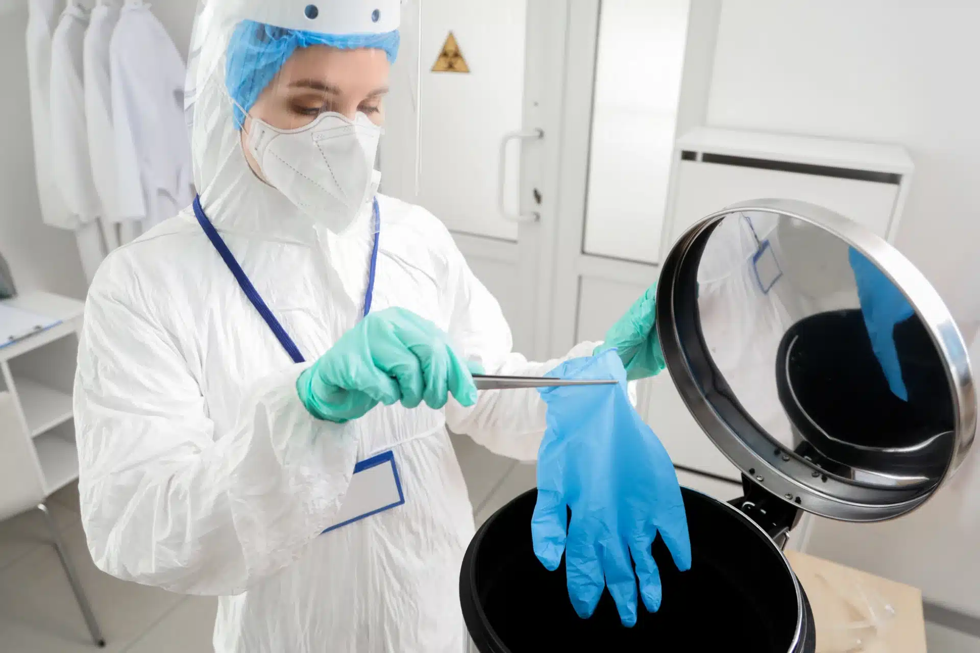 Medical waste management professional wearing PPE, throwing used gloves in a container