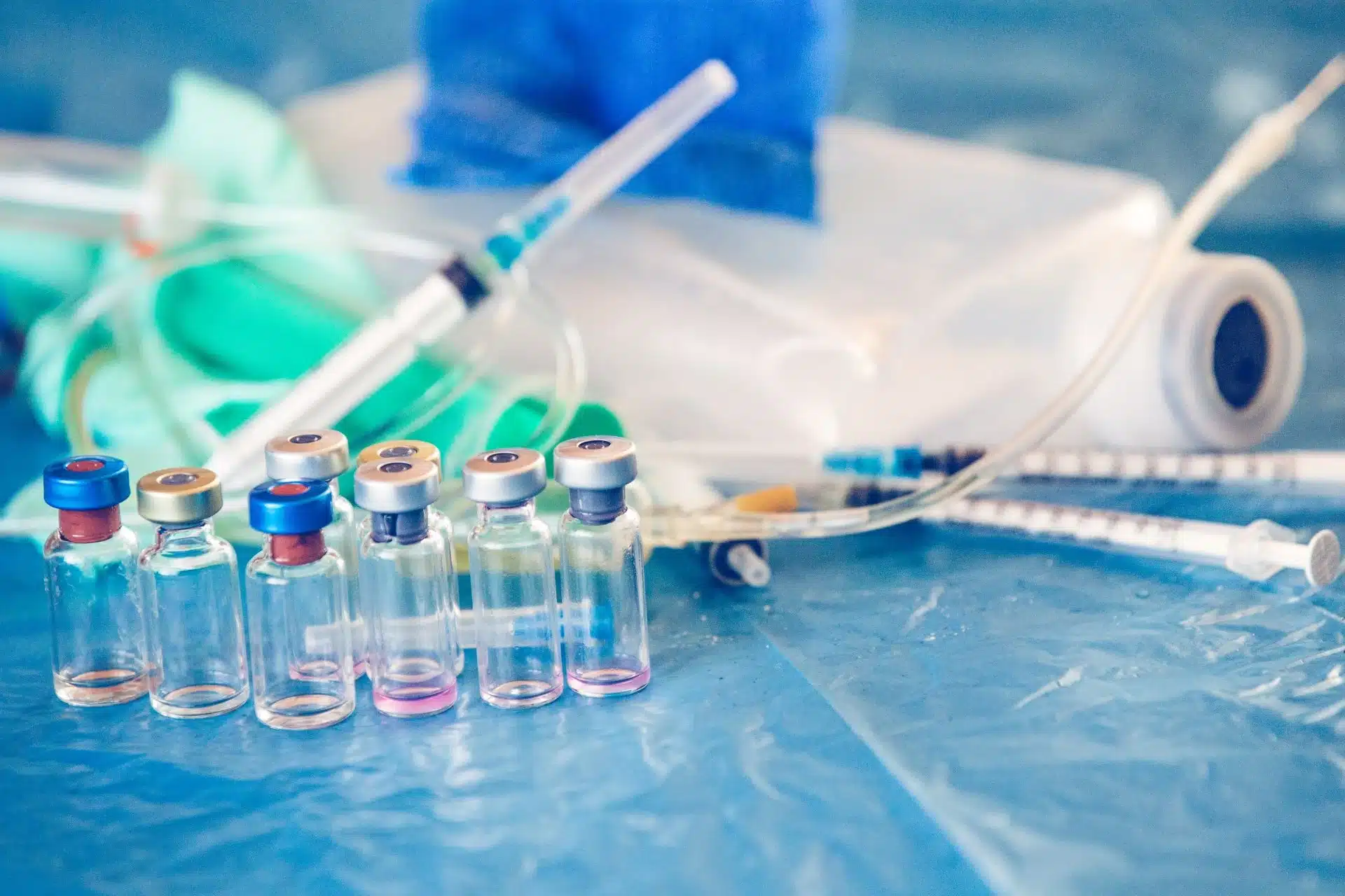 Row of glass vials with colored caps and pink liquid on a blue surface in a clinical setting.