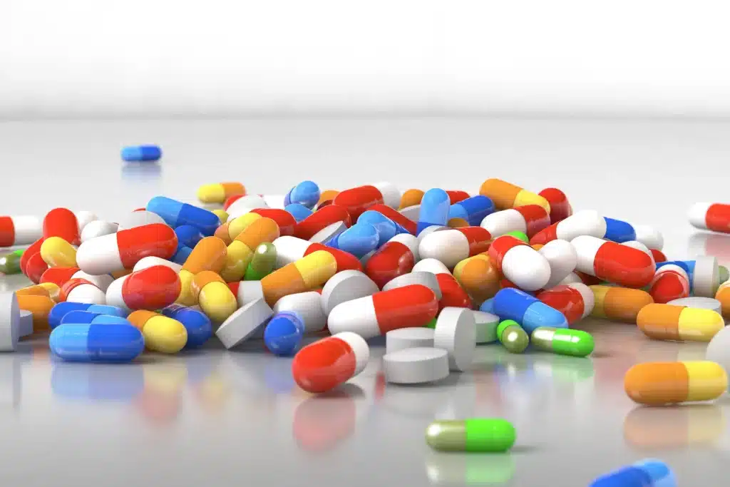 Assorted colorful pills and capsules scattered on a reflective surface.
